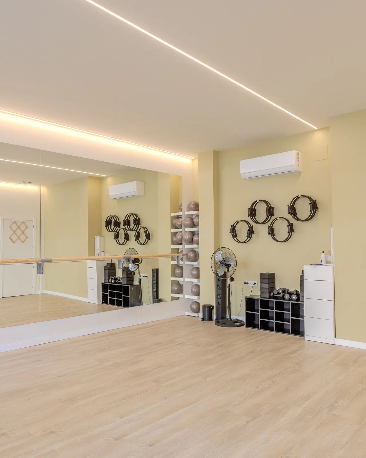 Sala de Barre y Pilates con pared de espejo, aros de pilates colgados y suelo de madera clara